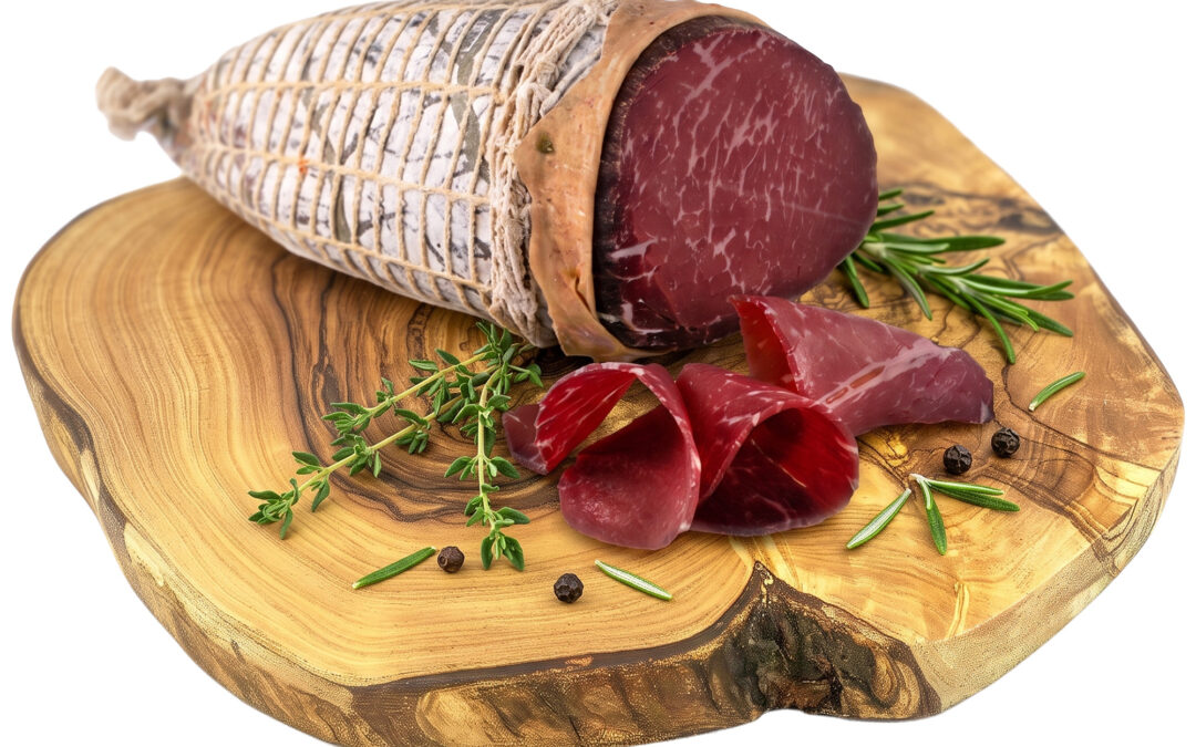 Whole cured ham leg on a wooden cutting board, tied with nets, with rosemary sprigs and peppercorns nearby and several slices showing.