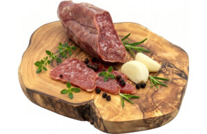 Sliced salami on a wooden cutting board with garlic cloves, rosemary, thyme, and black peppercorns nearby.