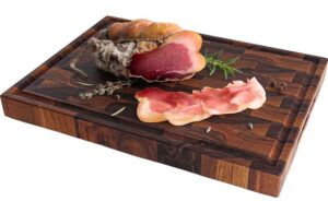 Cured ham with several slices on a dark wooden cutting board, rosemary sprigs nearby.