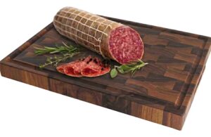 Whole salami with sliced pieces on a dark wooden cutting board, garnished with rosemary and thyme.