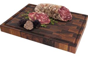 Sliced salami and black truffles arranged on a wooden cutting board with herbs nearby.