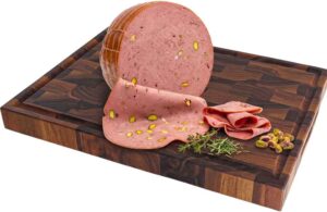 Mortadella with pistachios sliced on a dark wooden cutting board, with herbs and rolled slices nearby.