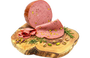 Mortadella loaf with pistachio pieces on a wooden board, with slices fanned out and herbs nearby.